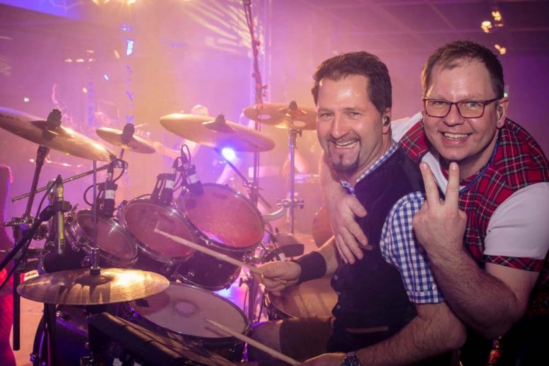 Gerry Grass und Andi Häckl posieren lachend vor dem Schlagzeug